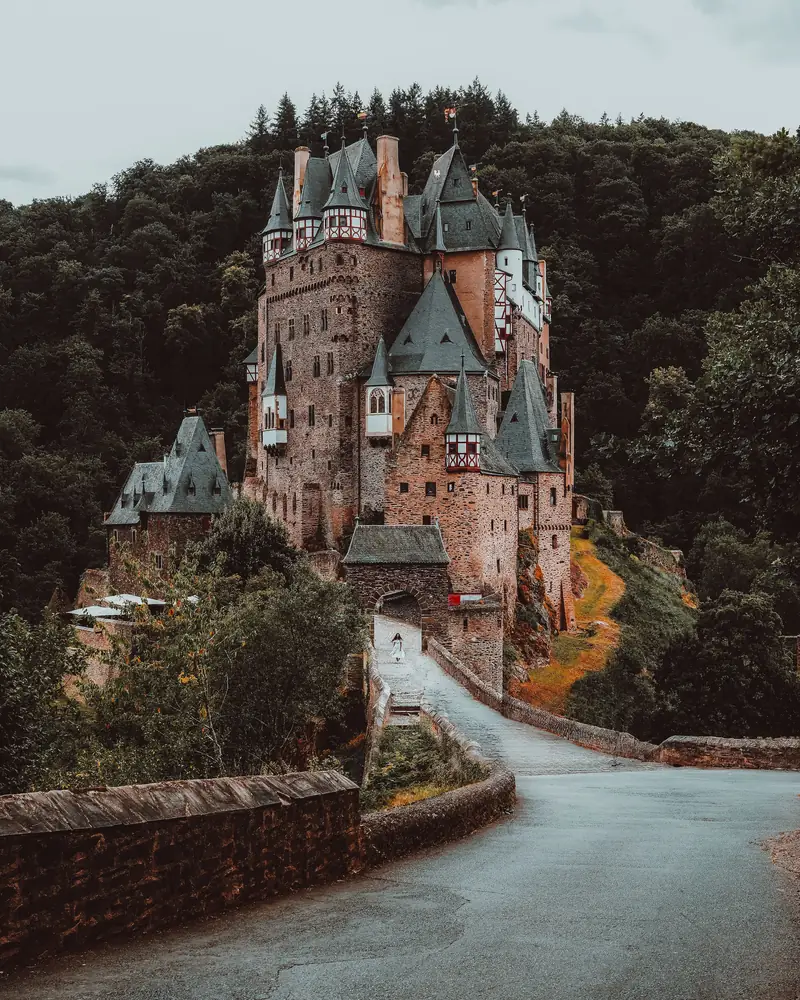 El castillo de Eltz entre árboles, con un camino curvo que sube hacia él.