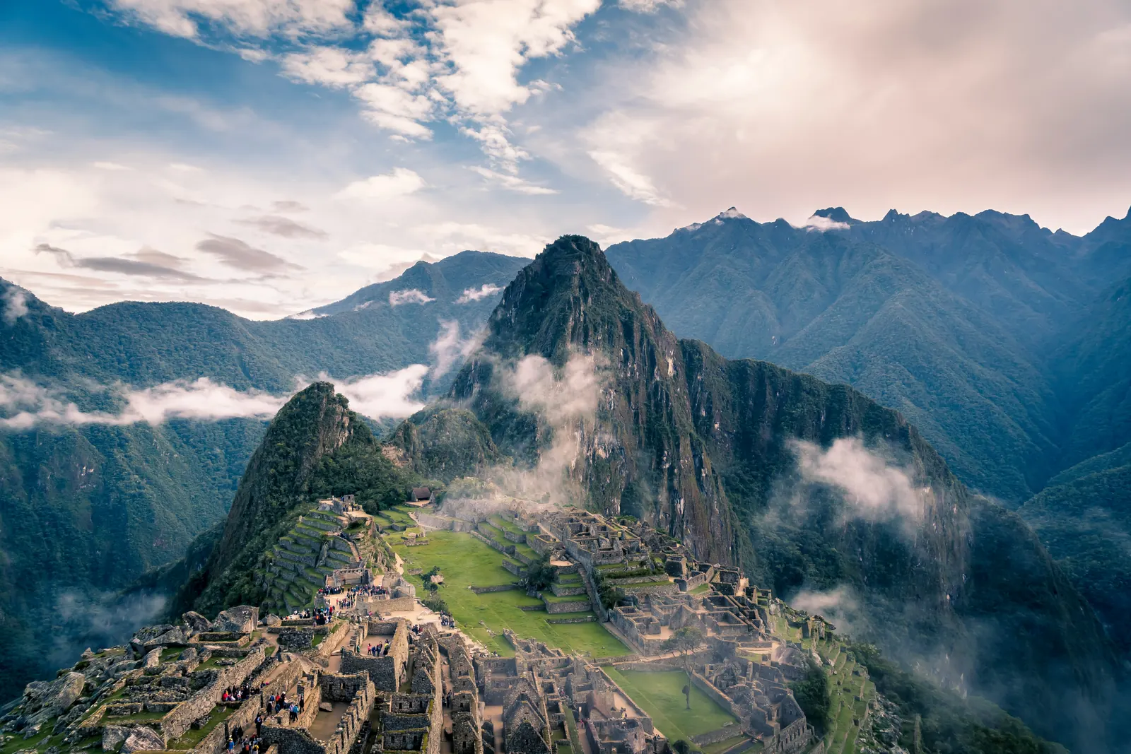 Vista de las ruinas de Machu Picchu con el monte Huayna Picchu al fondo, rodeado de nubes y montañas.